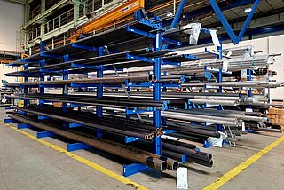 Shelf in a warehouse with long metal pipes in various diameters for the production of hydraulic piping systems.