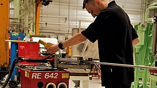 A man placing a steel pipe in a welding machine