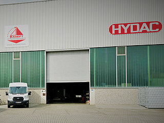 Exterior view of the KRAEFT company building, 2 cars and a delivery van are parked in front of the building in the foreground