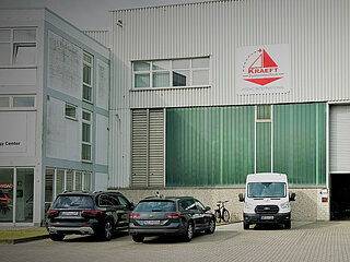 Exterior view of the KRAEFT company building, 2 cars and a delivery van are parked in front of the building in the foreground